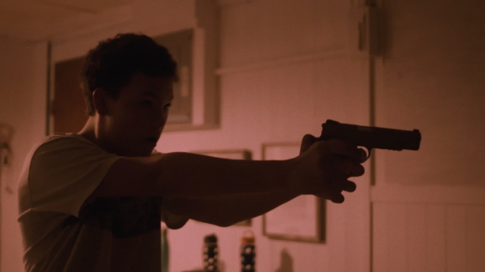 A boy raises a pistol with both hands in a pink-lit room